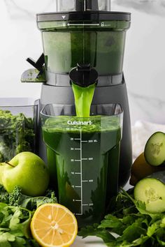 a juicer filled with green liquid surrounded by fruits and vegetables