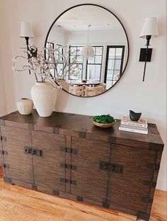 a large round mirror hangs on the wall above a dresser with drawers and vases