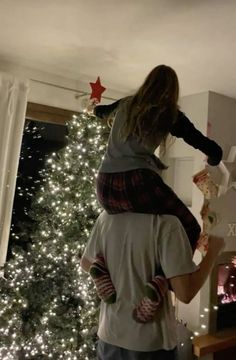 a man holding a child in his arms near a christmas tree with lights on it