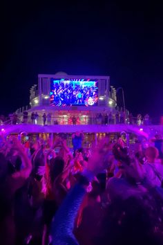 a crowd of people standing on top of a boat at night with their hands in the air