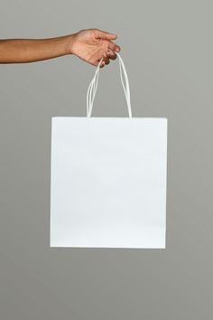 a person's hand holding a white paper shopping bag against a gray background with copy space