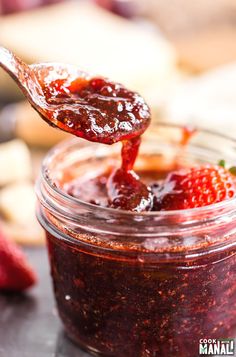 a spoon full of strawberry jam is being held up by someone's hand over the jar