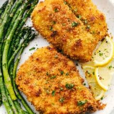 two pieces of fried chicken on a plate with asparagus and lemon wedges