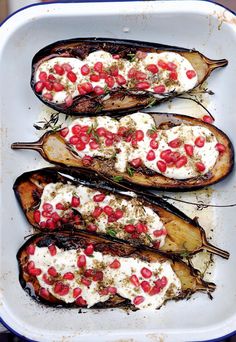 four baked eggplant boats with tomatoes and herbs on top in a baking pan