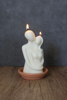 two candles sitting on top of a wooden table next to a bowl with a candle in it