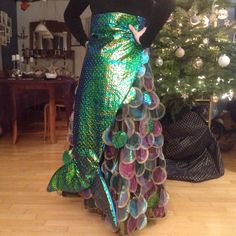 a woman in a mermaid costume standing next to a christmas tree