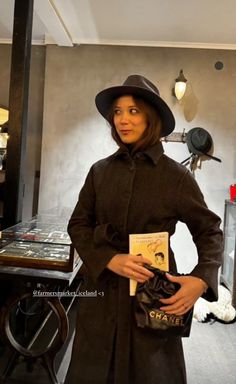 a woman wearing a coat and hat holding a book