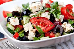 a salad with olives, tomatoes, cucumbers and feta cheese in a white bowl