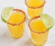 three glasses filled with yellow liquid and garnished with lime, sitting on a white surface