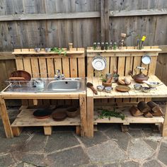 an outdoor kitchen made out of pallets and wooden crates with dishes on them, sitting next to a fence