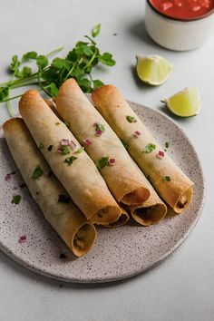 three burritos on a plate with salsa and cilantro