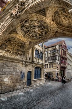 an arch in the middle of a street with people walking under it and buildings around