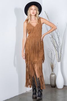 a woman wearing a brown fringe dress and black cowboy hat standing in front of a white wall