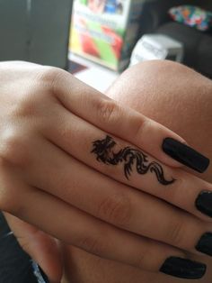 a woman's hand with a black dragon tattoo on her left thumb and finger