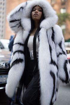 a woman is walking down the street wearing a white and black fur coat with hood