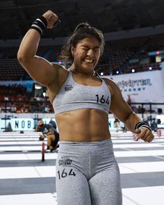 a woman with her arm raised in the air and wearing grey sports bra top, shorts and black wristbands