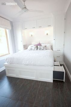 a white bed sitting in a bedroom on top of a hard wood floor next to a window