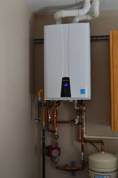 a tank mounted to the side of a wall next to a water heater and pipes