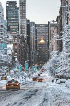 a city street covered in snow and surrounded by tall buildings with cars driving down it