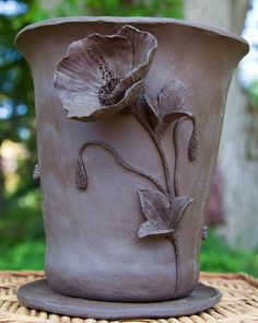 a clay vase with flowers on it sitting on a wicker table in front of some trees