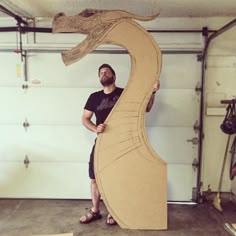 a man is standing next to a cardboard sculpture that looks like a sea horse in a garage