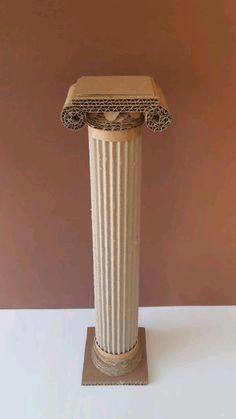 a tall white vase sitting on top of a wooden stand in front of a brown wall