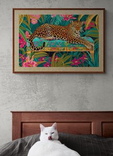 a white cat laying on top of a bed next to a framed wall art above it