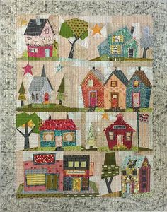 a quilted wall hanging with houses and trees on it's sides, all in different colors