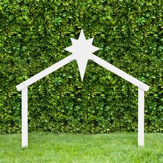 a white wooden nativity set in front of a green hedge with a star on top