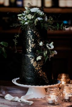 a black and gold wedding cake with white flowers on the top is surrounded by candles