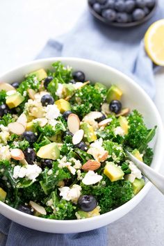 a white bowl filled with blueberries, broccoli and feta cheese next to lemon wedges