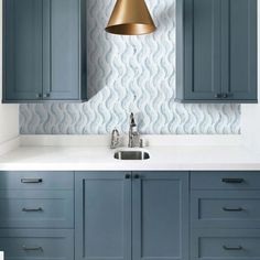 a kitchen with blue cabinets and gold pendant light over the sink in front of it