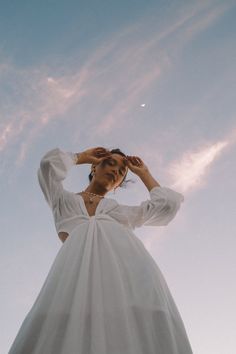 a woman in a white dress standing under a blue sky