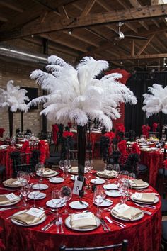 a red table cloth with white feathers and place settings on it is set for an event