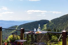 an outdoor table with two chairs and a bottle of wine on it overlooking the mountains