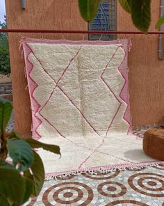 a white and pink quilt sitting on top of a wooden chair next to a tree