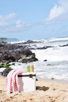 a cooler sitting on top of a sandy beach next to the ocean with a towel draped over it