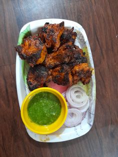 there is a plate with some chicken wings and onion rings next to a small bowl of green sauce