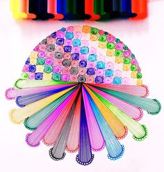 several different colored paper fan sitting on top of a white table next to crayons