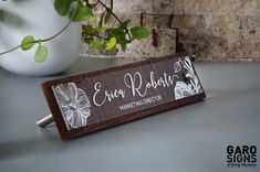 a wooden sign sitting on top of a table next to a potted plant