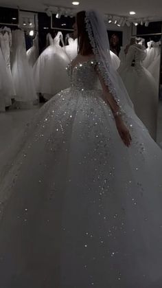 a woman in a white wedding dress looking at dresses on mannequins behind her