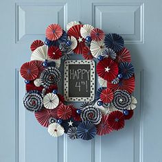 a fourth of july wreath hanging on a blue door with red, white and blue paper fans