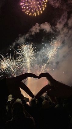 two people making a heart with their hands in front of fireworks