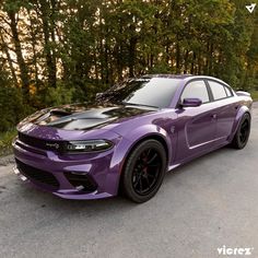 the purple dodge charger is parked on the side of the road in front of some trees