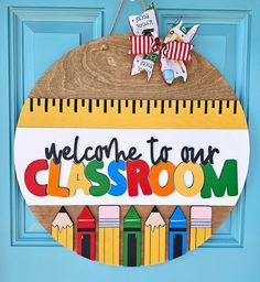 a welcome to our classroom sign hanging on a blue door with pencils and ruler