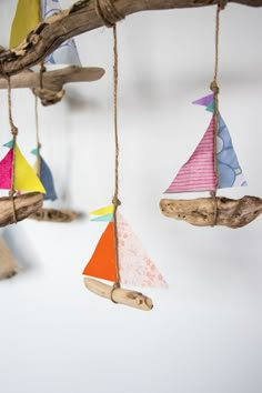 colorful sailboats are hanging from the branches of a tree branch, and they're made out of driftwood