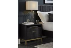 a night stand with a lamp on top of it next to a bed and pillows