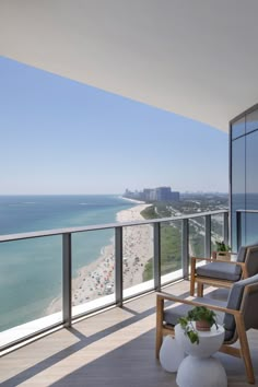 a balcony overlooking the beach and ocean with chairs, potted plant and large windows