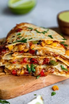 a stack of quesadillas sitting on top of a cutting board next to sliced limes