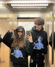 two people standing in front of an elevator taking a selfie with their cell phone